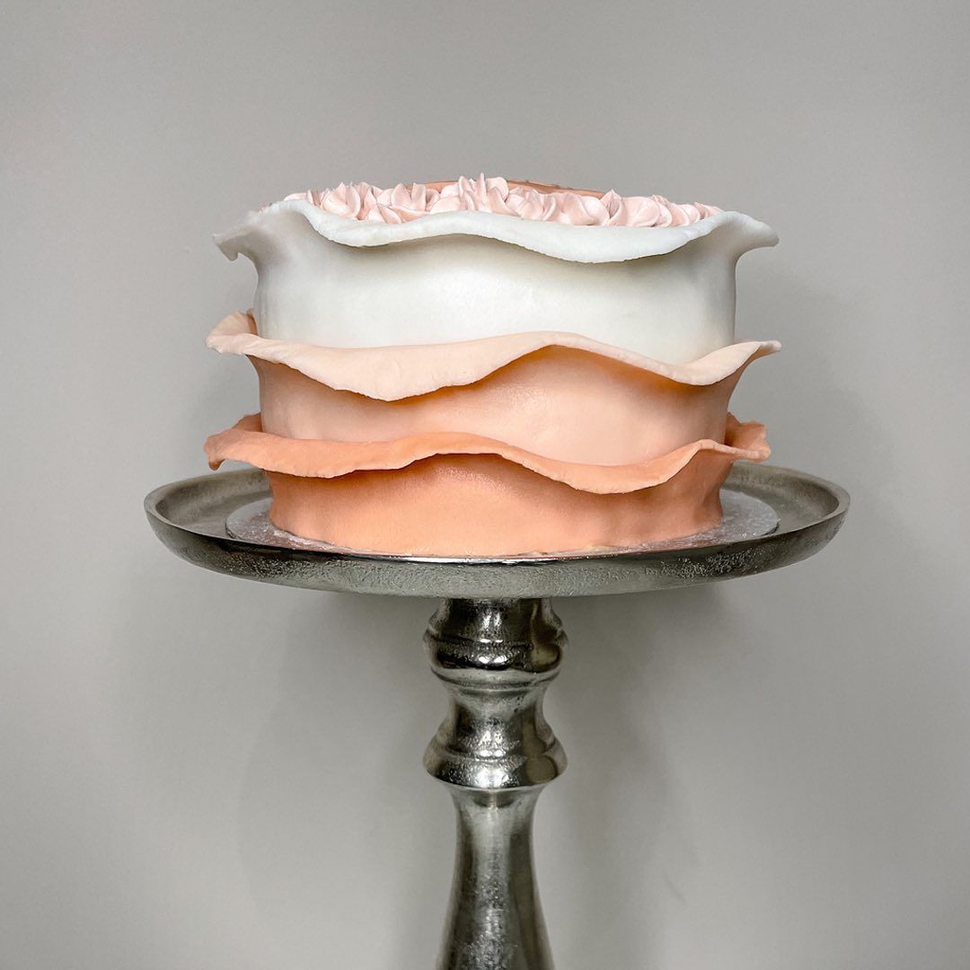 An ombre peach ruffle cake on a silver stand
